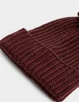 Gorro de lana tejido a crochet en color beige con detalles en blanco y pompón de piel sintética en la parte superior.
