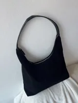 Cartera tipo hobo de gamuza sintética color negro, con cierre dorado y correa de hombro de cuero sintético. Tiene compartimentos internos, uno de ellos con cierre.