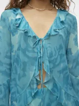 Camisa celeste con estampado de flores, cuello en V, cierre de cordón y volantes en los puños.