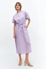 Vestido midi lila de lino, corte recto con tajos laterales, mangas cortas abullonadas con detalle de tablas en el puño y lazo en la cintura.