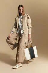 Trench color beige de corte clásico con cuello amplio, botones frontales, detalles en los hombros y mangas largas.