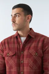 Sobrecamisa de algodón para hombre con interior de corderito, estampado a cuadros en tonos negro, blanco y azul. Tiene cierre de botones, bolsillos tipo cartera y logo en goma. El modelo usa talle M.