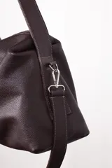 Bolso tipo hobo color borgoña, de cuero con textura granulada. Tiene correa de hombro ajustable y extraíble, cierre superior con cremallera, forro interior de algodón con bolsillo con cremallera y bolsillo abierto.