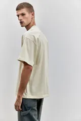 Remera color crema de algodón de peso medio, con cuello redondo ribeteado, hombros caídos, corte oversized y bajo recto.