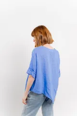 Blusa color naranja confeccionada en 100% lino, con escote en V, mangas cortas con vuelta y silueta amplia. Presenta terminación asimétrica y fila de botones decorativos en uno de los hombros.
