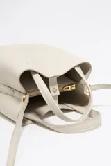 Bolso tote pequeño de piel reconstituida color gris claro, con estructura rígida, doble asa corta, correa extraíble, cierre con botón de presión, logo metálico BIMBA Y LOLA, acabados metálicos, bolsillo interior con cierre de cremallera e interior con logo grabado.