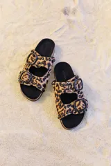 Sandalia tipo birkenstock de pelo con estampado animal print (leopardo), con dos tiras ajustables con hebillas negras y tachas metálicas negras. La plantilla es de corcho y la suela de goma eva.