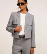 Blazer corto gris de poliéster y elastano, con solapas en el escote y cierre con gancho. Presenta bolsillos delanteros y corte horizontal en la espalda.