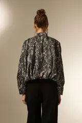Campera estilo bomber de manga larga, con cuello mao y cierre frontal. Confeccionada en tejido de poliéster con estampado de piel de serpiente en tonos grises y negros.