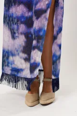 Vestido largo con estampado abstracto en tonos azul, lila y blanco. Tiene cuello mao con abertura en forma de lágrima, mangas largas acampanadas, espalda abierta, tajo frontal y flecos en el ruedo.