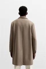 Abrigo recto color beige confeccionado en tejido con lana. Tiene cuello con solapas de muesca, manga larga con puños abotonados, bolsillos de vivo en la cadera, bolsillo interior, abertura en el centro de la espalda y cierre frontal con botonadura.