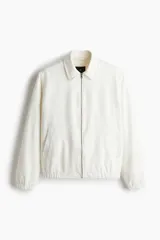 Campera blanca de denim rígido con cuello clásico, cierre frontal con cremallera, bolsillos laterales y un bolsillo interior. Tiene elástico en puños y bajo. Corte estándar y forro interior.