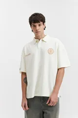 Remera polo color beige con textura acanalada, corte oversize, cuello clásico con botones y logo estampado en el pecho.