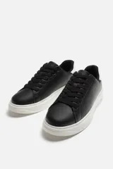 Zapatillas deportivas negras con detalle en blanco en la parte posterior y suela blanca con volumen de diseño irregular.