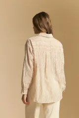 Camisa de manga larga color beige claro con bordado de flores blancas en relieve, cuello clásico y corte holgado.