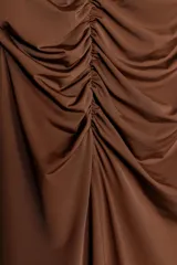 Falda midi color marrón chocolate, de tiro alto con cintura elástica, detalle de frunces en un lateral y abertura frontal.