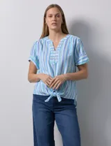 Blusa de algodón estampado a rayas verticales en tonos celeste, azul y verde. Tiene cuello a la base, escote en V con bordado y botones. Terminación de ruedo con nudo.