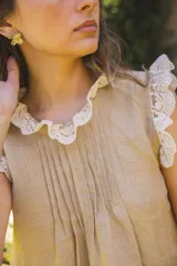 Blusa de lino color blanco, sin mangas, con cuello fruncido y volados de encaje en las sisas. Presenta pinzas frontales y un diseño de calce holgado de estilo romántico.