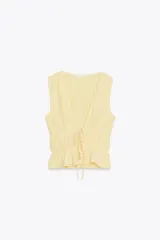 Top amarillo con estampado de cuadros vichy blancos, escote en pico, sin mangas, con detalle de elásticos en la cintura y cierre frontal con lazadas.