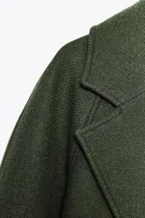 Abrigo largo color verde militar confeccionado en lana. Tiene cuello solapa, manga larga, bolsillos laterales y cinturón lazada en el mismo tejido. El forro interior es combinado a contraste.