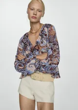 Blusa de gasa estampada con motivos paisley en tonos marrón, celeste y rosa. Tiene escote en V con volantes, mangas largas con puños elásticos y corte holgado.