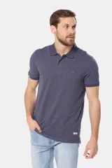 Polo de piqué color azul oscuro con un mini estampado geométrico repetitivo en todo el cuerpo. Presenta cuello y tapeta de botones en color liso, y un pequeño logo bordado en el pecho.