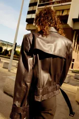 Cazadora biker de cuero color marrón oscuro, con cuello solapa de muescas, doble botonadura cruzada, cinturón ajustable con hebilla y mangas largas con cintas ajustables con hebilla.