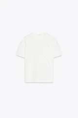 Camiseta blanca de algodón de manga corta y cuello redondo con detalle de flores en relieve en el frente.