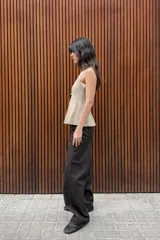 Top de punto acanalado en color beige, sin mangas y con cuello redondo. Presenta un cierre frontal con botones pequeños y un bajo con acabado en peplum que aporta volumen.