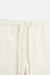 Pantalón negro de corte cropped, con cintura elástica ajustable con cordón, bolsillos laterales y traseros de vivo. El bajo tiene terminación con vuelta.