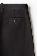 Pantalón negro de corte slim fit, confeccionado en sarga elástica de algodón. Cuenta con cierre y botón, bolsillos al bies y bolsillos insertados atrás con botón.