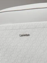 Cartera tipo camera bag de color blanco/gris claro, confeccionada en piel sintética con textura de monograma en el bolsillo frontal. Cuenta con dos correas desmontables: una ancha y otra fina, ambas ajustables. El bolsillo frontal tiene el logo de Calvin Klein en metal plateado.