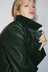 Blazer de piel color verde oscuro, de corte cruzado con doble botonadura negra, cuello solapa de muescas y manga larga.