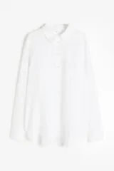 Camisa blanca de lino con cuello clásico, abotonada al frente, de manga larga con puños abotonados, canesú en la espalda, bolsillo de parche en el pecho y bajo redondeado.