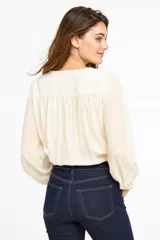 Blusa de poliéster con estampado abstracto en tonos beige y negro, escote en V con frunce, mangas largas abullonadas con puños elásticos y corte a la cintura con elástico.