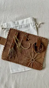 Set de accesorios de metal dorado con detalles en cuero marrón, que incluye un brazalete, aros, un collar y un broche. Se presenta en un sobre de cuero marrón con cierre de broche.