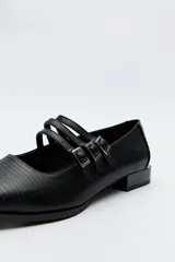 Zapato tipo Mary Jane color negro con textura de reptil, de charol sintético con punta cuadrada y triple tira con hebillas.