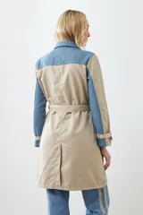 Trench largo color beige con secciones en denim azul, cuello camisero, cierre frontal con botones y bolsillos con solapa en el pecho.