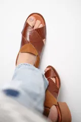 Sandalias de cuero marrón con tiras cruzadas en el empeine y tira alrededor del tobillo.