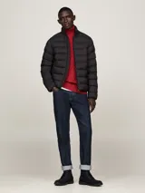 Campera acolchada negra de nailon con aislamiento térmico y acabado repelente al agua. Tiene cuello alto, cierre de cremallera, dos bolsillos delanteros y parche engomado del logo de Tommy Hilfiger en la manga.