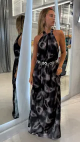 Vestido largo estampado en tonos negro, gris y rosado, con cuello halter drapeado y caída fluida. Se complementa con un cinturón metálico de eslabones circulares.