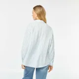 Camisa celeste y blanca a rayas verticales, de corte holgado, manga larga y bolsillo de parche en el pecho.