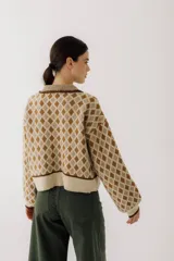 Sweater de punto color beige con diseño de rombos marrones, cuello polo con botones y mangas largas abullonadas.