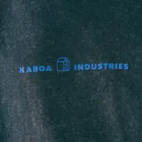 Remera oversize gris con efecto gastado y estampado frontal con el texto "KABOA INDUSTRIES" en azul.
