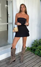 Vestido corto negro, sin mangas y con escote recto (strapless). La falda tiene un diseño con volados superpuestos.