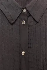 Camisa oversize color marrón oscuro confeccionada en tejido satinado con efecto arrugado, cuello solapa, manga larga con puños y cierre frontal con botones metálicos.