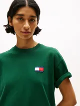 Remera verde de algodón con cuello redondo y corte amplio. Presenta el logo de Tommy Hilfiger en el pecho y un logo oversize en la parte trasera. Tiene mangas cortas con hombros caídos y un parche con logo en la manga.