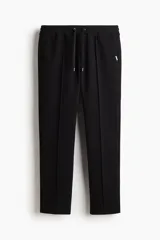 Pantalón tipo jogger negro, de corte recto y silueta clásica, confeccionado en tejido de punto de mezcla de algodón. Presenta pliegue cosido frontal, cintura elástica con cordón ajustable y bolsillos laterales y trasero insertado.