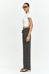Pantalón recto de viscosa color negro con estampado de flores pequeñas en blanco. Tiene tiro bajo, elástico en la cintura y bolsillos al bies.