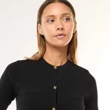 Vestido corto negro de punto grueso con botones dorados al frente, cuello redondo y mangas cortas. Presenta bolsillos de parche a la altura del busto y en la falda.